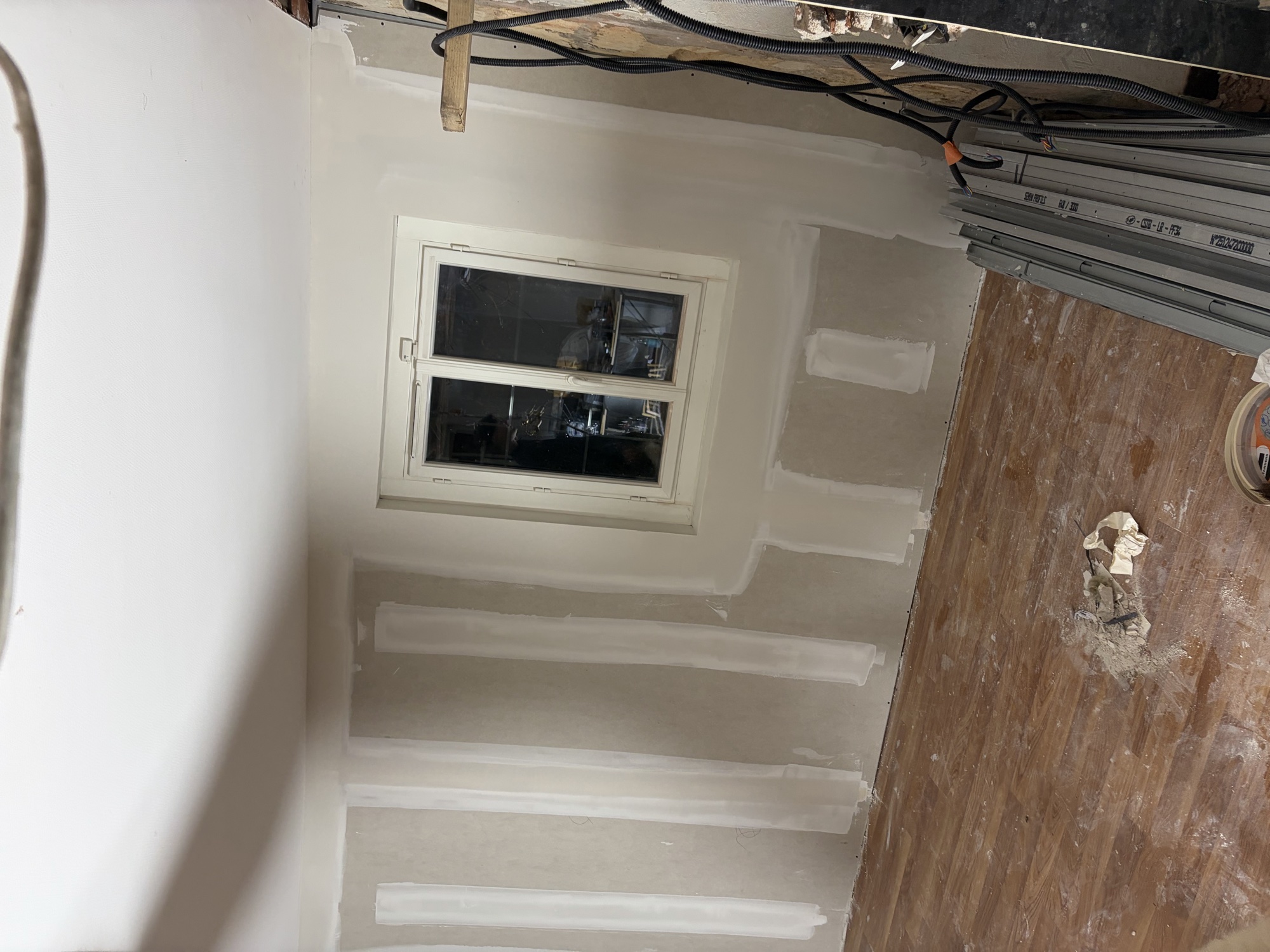 Murs en placo avec bandes à joint autour d'une fenêtre, rails au sol, chantier intérieur